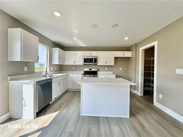 kitchen with a textured ceiling, stainless steel appliances, sink, white cabinets, and a center island