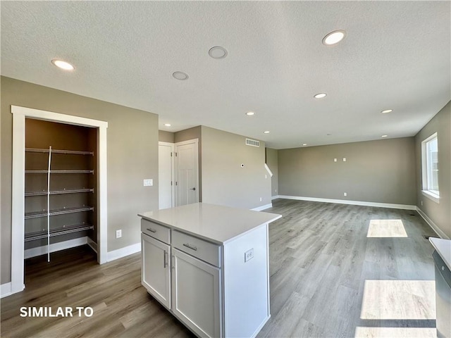 kitchen featuring light wood-type flooring, a textured ceiling, built in features, white cabinets, and a center island