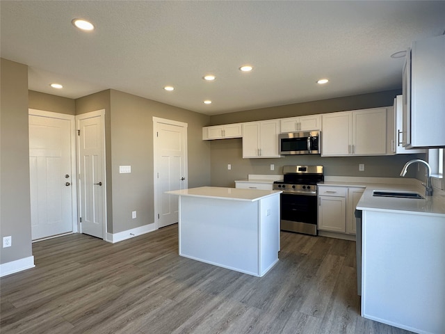 kitchen featuring wood finished floors, baseboards, a kitchen island, a sink, and stainless steel appliances