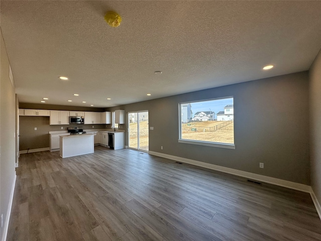 unfurnished living room featuring recessed lighting, a textured ceiling, baseboards, and dark wood-style flooring