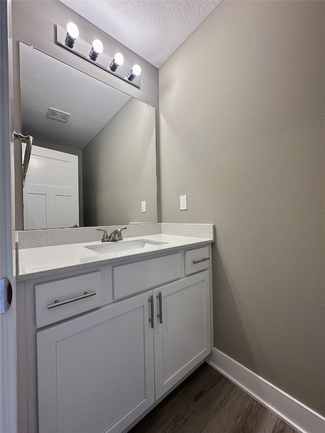 bathroom featuring visible vents, baseboards, vanity, wood finished floors, and a textured ceiling