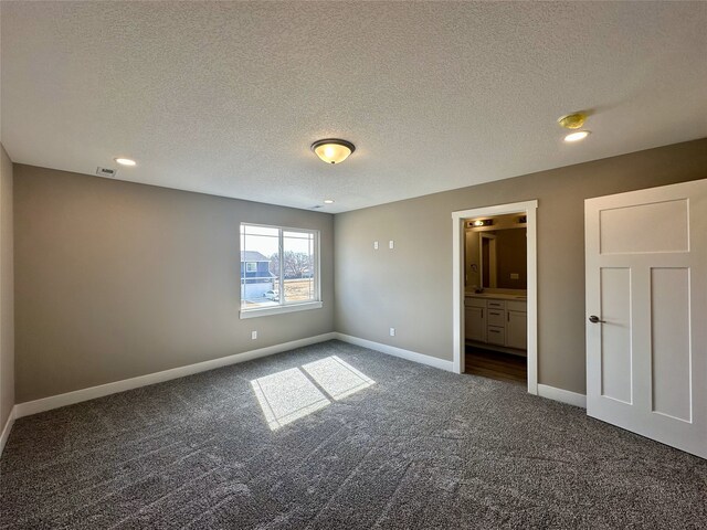 unfurnished bedroom featuring visible vents, a textured ceiling, ensuite bath, dark carpet, and baseboards