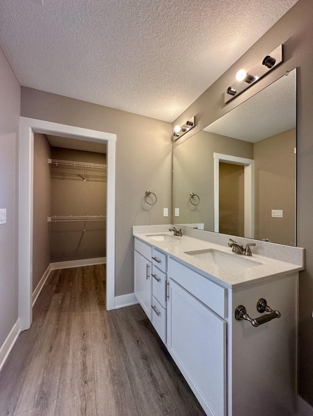 full bathroom with a sink, a textured ceiling, wood finished floors, double vanity, and baseboards