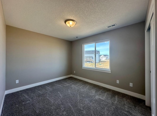 empty room featuring visible vents, dark carpet, a textured ceiling, and baseboards