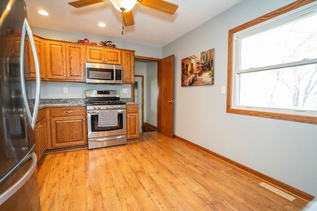 kitchen featuring stainless steel appliances, dark stone counters, light wood-type flooring, a textured ceiling, and ceiling fan