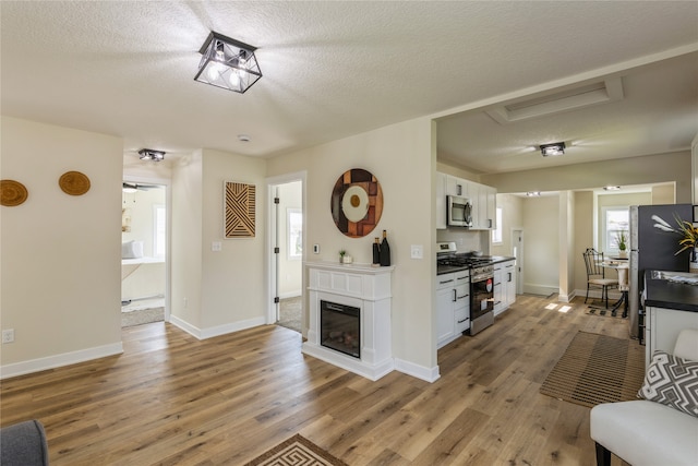 living room with ceiling fan, a textured ceiling, and light hardwood / wood-style flooring