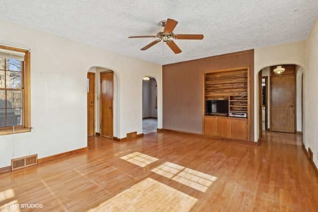 unfurnished living room featuring hardwood / wood-style floors, built in features, a textured ceiling, and ceiling fan