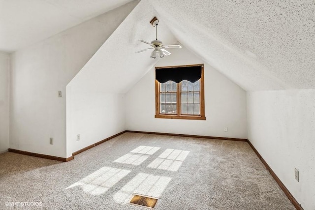 additional living space with ceiling fan, light colored carpet, vaulted ceiling, and a textured ceiling