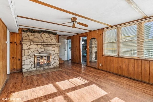 unfurnished living room with beamed ceiling, wooden walls, wood-type flooring, and a stone fireplace