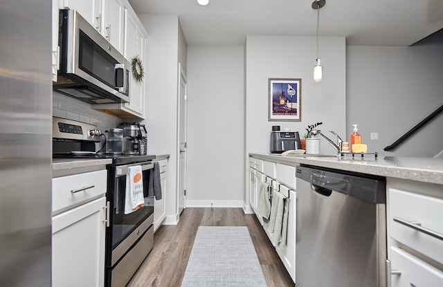 kitchen featuring white cabinetry, appliances with stainless steel finishes, backsplash, hanging light fixtures, and hardwood / wood-style floors