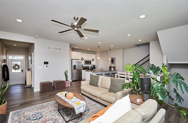 living room featuring dark wood-type flooring, a textured ceiling, and ceiling fan