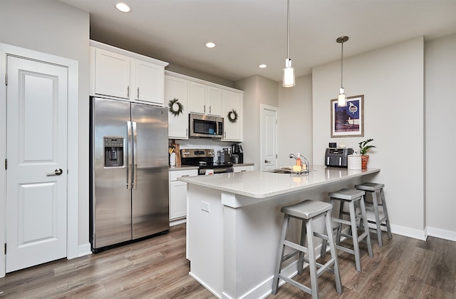 kitchen featuring sink, kitchen peninsula, appliances with stainless steel finishes, decorative light fixtures, and white cabinets