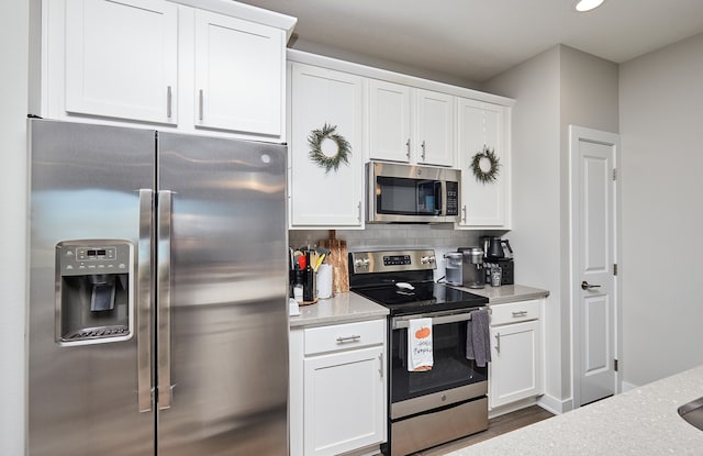 kitchen featuring stainless steel appliances, white cabinetry, dark hardwood / wood-style flooring, light stone countertops, and decorative backsplash