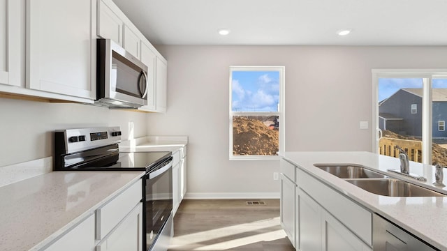 kitchen featuring sink, appliances with stainless steel finishes, white cabinetry, light stone countertops, and light hardwood / wood-style floors