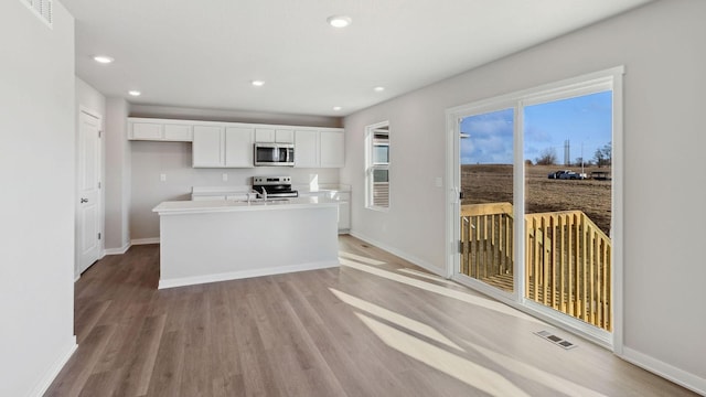 kitchen featuring stainless steel appliances, white cabinetry, an island with sink, and light hardwood / wood-style floors