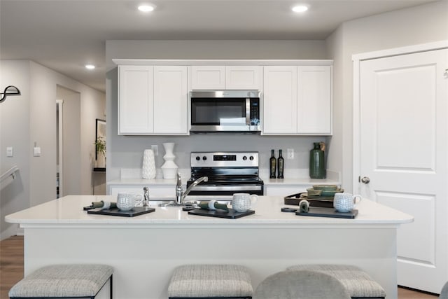 kitchen with white cabinetry, stainless steel appliances, a kitchen bar, and a kitchen island with sink