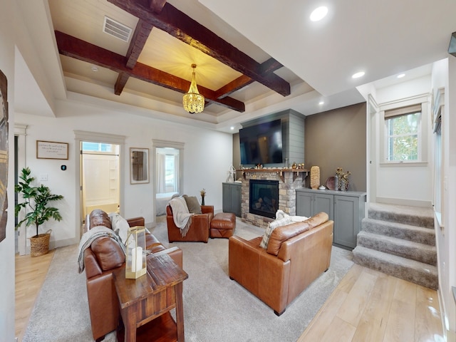 living room with beamed ceiling, a stone fireplace, light hardwood / wood-style flooring, and coffered ceiling