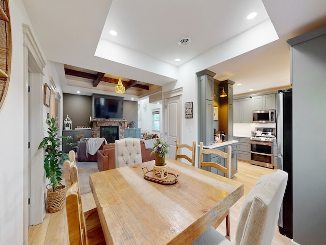 dining area featuring light wood-type flooring, beam ceiling, and a raised ceiling