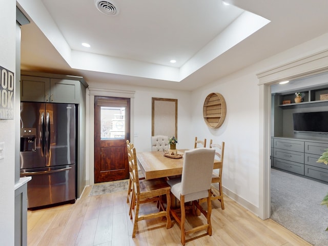 dining space with light wood-type flooring and a tray ceiling