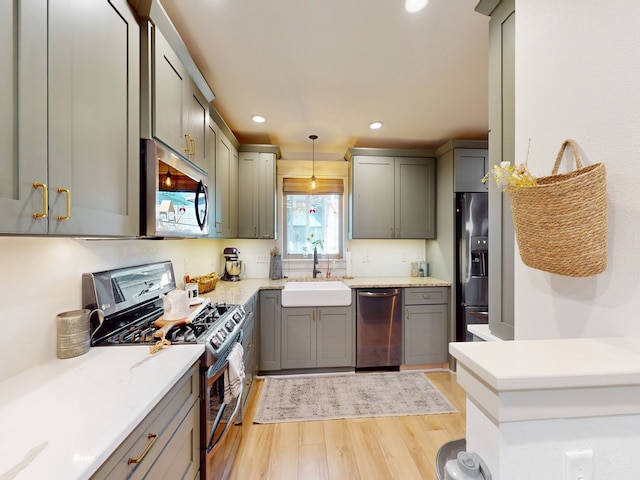 kitchen with stainless steel appliances, light hardwood / wood-style floors, sink, gray cabinets, and pendant lighting