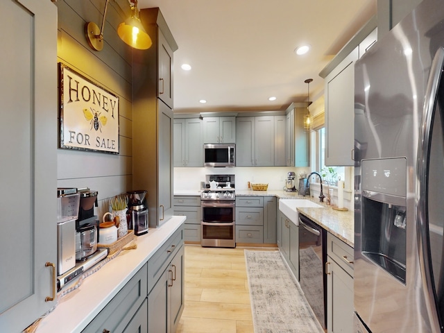 kitchen with hanging light fixtures, gray cabinets, light wood-type flooring, and stainless steel appliances