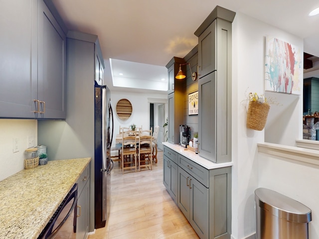 kitchen featuring light stone countertops, light hardwood / wood-style floors, stainless steel refrigerator, and gray cabinetry