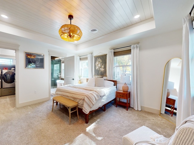 carpeted bedroom featuring washing machine and clothes dryer, a raised ceiling, wooden ceiling, and ensuite bath