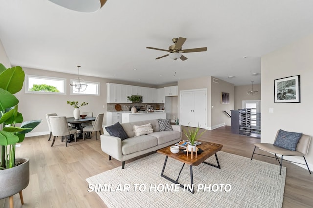 living area featuring baseboards, ceiling fan with notable chandelier, and light wood finished floors