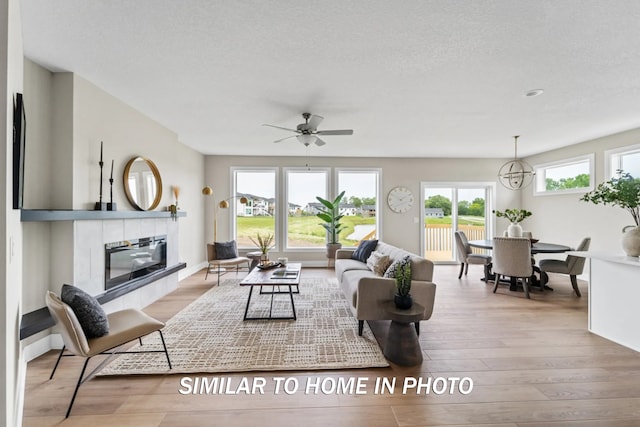 living room with a textured ceiling, a ceiling fan, wood finished floors, and a tile fireplace