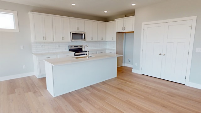 kitchen with an island with sink, decorative backsplash, white cabinets, stainless steel appliances, and a sink