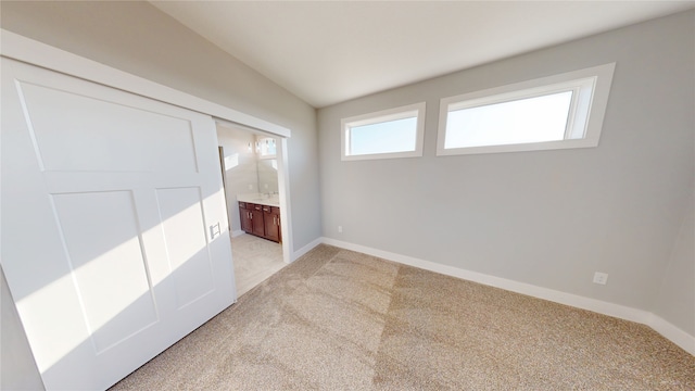 unfurnished bedroom with connected bathroom, baseboards, and light colored carpet