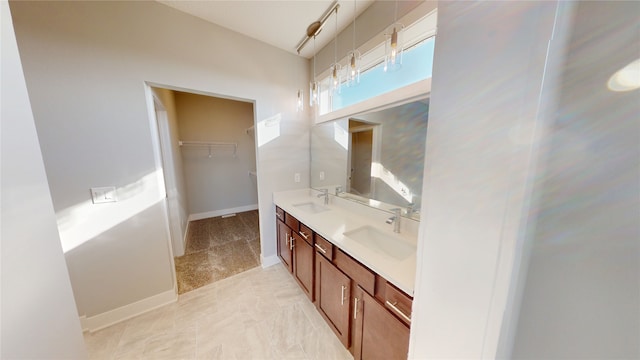 full bath with double vanity, a walk in closet, baseboards, and a sink