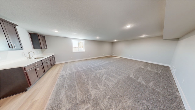 basement featuring light wood finished floors, baseboards, recessed lighting, a textured ceiling, and a sink