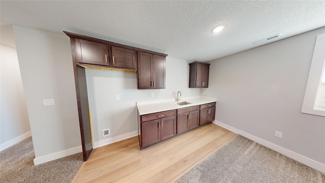 kitchen with visible vents, dark brown cabinets, baseboards, light countertops, and a sink