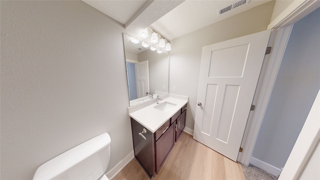 bathroom with vanity, wood finished floors, visible vents, baseboards, and toilet