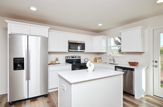 kitchen featuring appliances with stainless steel finishes, sink, light hardwood / wood-style floors, white cabinets, and a center island