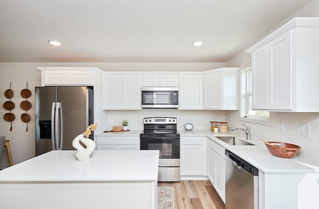 kitchen with stainless steel appliances, white cabinetry, sink, light hardwood / wood-style flooring, and a center island