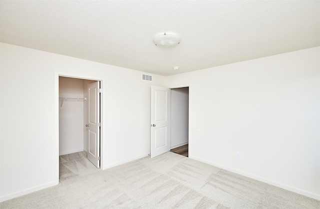 unfurnished bedroom with light colored carpet, a walk in closet, and a closet