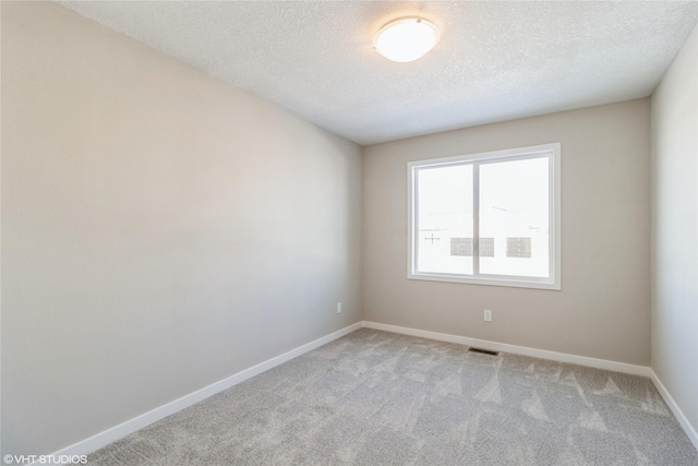 empty room with a textured ceiling, carpet flooring, visible vents, and baseboards