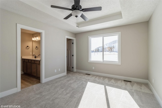 unfurnished bedroom featuring a raised ceiling, light carpet, a textured ceiling, and baseboards