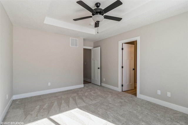 unfurnished bedroom with a tray ceiling, carpet, visible vents, a textured ceiling, and baseboards