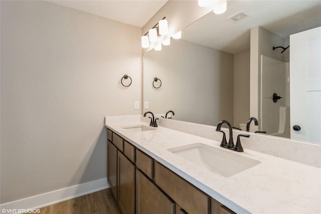 full bath with double vanity, baseboards, a sink, and wood finished floors