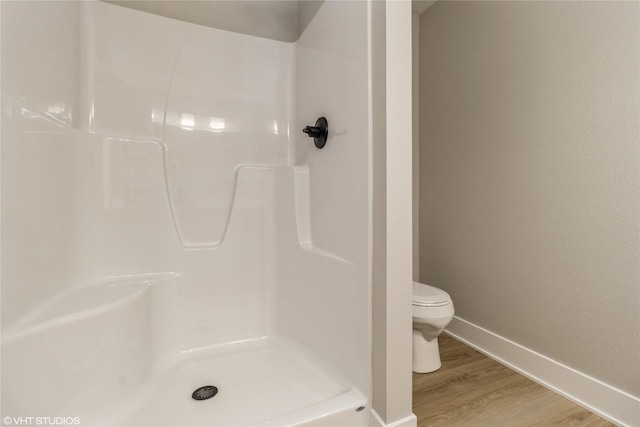 bathroom featuring baseboards, walk in shower, toilet, and wood finished floors