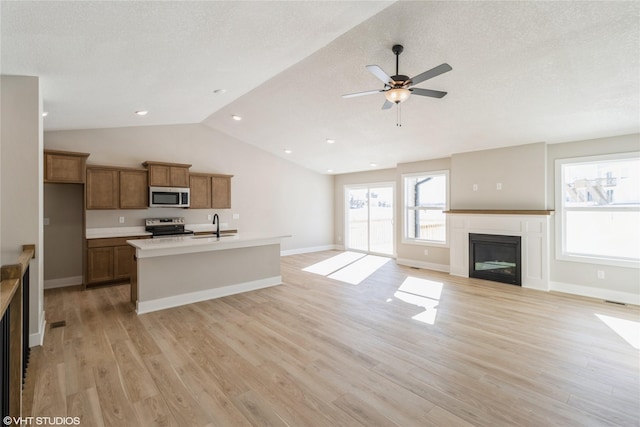 kitchen with open floor plan, appliances with stainless steel finishes, light wood-type flooring, brown cabinetry, and a glass covered fireplace