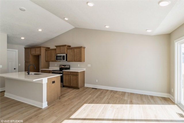 kitchen with brown cabinets, a kitchen island with sink, stainless steel appliances, light wood-style floors, and a sink