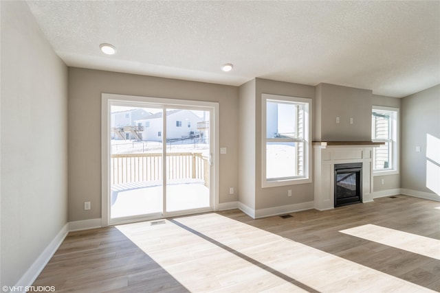 unfurnished living room featuring a glass covered fireplace, plenty of natural light, light wood-style flooring, and baseboards