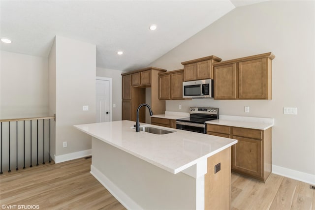 kitchen with a center island with sink, appliances with stainless steel finishes, brown cabinets, light wood-type flooring, and a sink