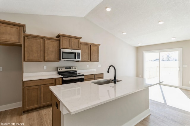 kitchen with appliances with stainless steel finishes, light wood-style floors, vaulted ceiling, and a sink