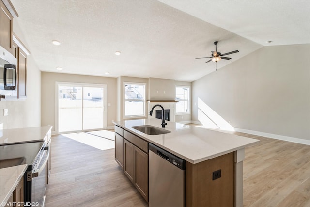 kitchen featuring a center island with sink, appliances with stainless steel finishes, open floor plan, a sink, and light wood-type flooring