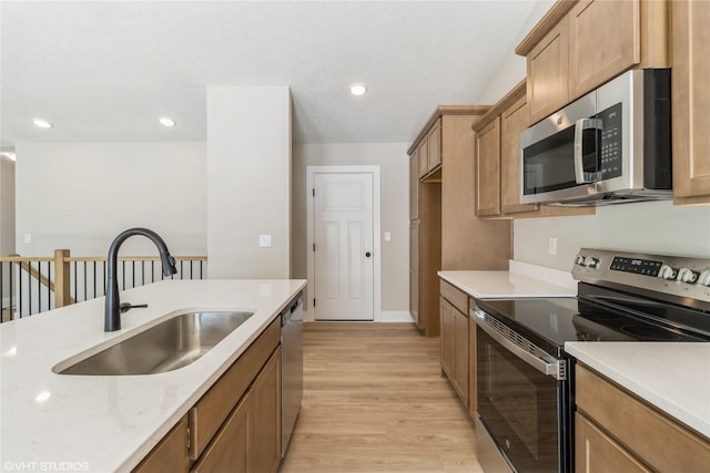 kitchen with light wood finished floors, brown cabinetry, stainless steel appliances, a sink, and recessed lighting